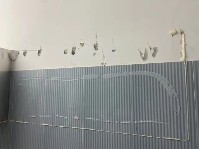 청회색 골무늬 타일 벽 위쪽 흰 벽면에 떼어낸 흔적과 실리콘 자국이 보이고 타일 표면에 접착 흔적이 남아 있는 실내 벽면